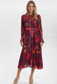 Lång bordeauxfärgad klänning med blommönster i rött och rosa, med knapplås framtill och midjebälte. Långa ärmar med manschettdetalj.