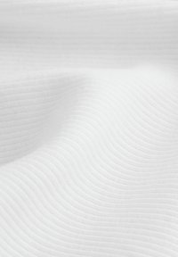 Texturiertes weißes Gewebe mit einem wellenförmigen Muster, das weiche Wellen über die Oberfläche zeigt. Glatte Oberfläche mit leichtem Erscheinungsbild.