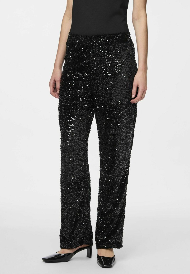 Pantalons en sequins noirs à coupe droite et taille élastique, avec une surface brillante et texturée. Associés à des chaussures à talons noires.