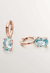 Pendientes de aro en oro rosa con una piedra ovalada facetada de color azul claro, con un acabado suave y un cierre seguro. Acompañados de una piedra de acento más pequeña.