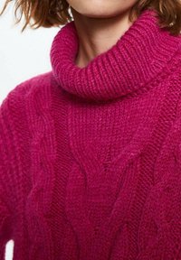 Femme portant un épais pull à col roulé magenta en maille torsadée avec un col côtelé, montrant le cou et une partie du visage.