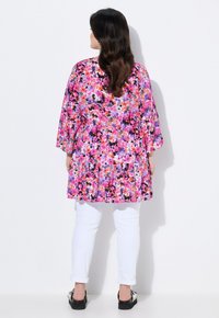 Bloem blouse in levendig roze, paars en zwart, met een peplum ontwerp en driekwart mouwen, gecombineerd met witte opgerolde broek.