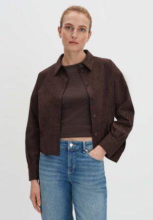 Bruine suède cropped jas met een kraag, lange mouwen en knoopsluiting. Draagt over een donkere tanktop en lichtblauwe jeans.