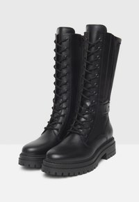 Ein Paar schwarze Leder-Knöchelhohe Kampfstiefel mit robusten Profilsohlen, frontalen Schnürsenkeln und seitlichen Reißverschlüssen auf einem weißen Hintergrund.