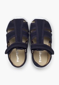 Tummansiniset sandaalit, joissa on elastiset hihnat ja tarrakiinnitys. Valkoinen kuminen varvaskorko ja pohja. Sisäpuolella on brändin logo hopeisena.