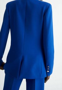 Królewski niebieski, dopasowany blezer o strukturalnym kroju, z pojedynczym rozcięciem, gładką tkaniną i złotymi guzikami na mankietach.