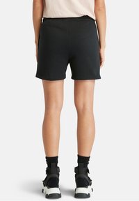 Shorts en coton noir avec une taille élastique, design simple, longueur mi-cuisse, assortis à des chaussures noires et blanches.