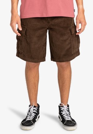 Brązowe sztruksowe krótkie spodenki cargo z bocznymi kieszeniami i prostym krojem, zestawione z czarnymi trampkami za kostkę i różowym t-shirtem.