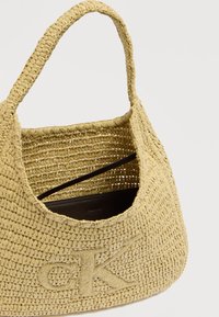 Ανοιχτό κίτρινο πλεκτό ψάθινο τσαντάκι με στρογγυλεμένο σχήμα, διακοσμημένο με ανάγλυφο λογότυπο "CK". Το εσωτερικό έχει σκουρόχρωμη επένδυση και διπλούς ιμάντες.