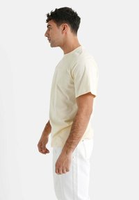 Lys gul bomulds-t-shirt med korte ærmer, rund halsudskæring og en afslappet pasform. Stoffet ser blødt og glat ud i teksturen.