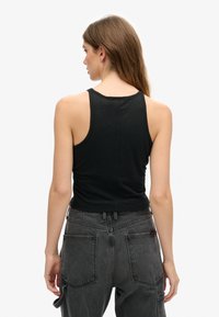 Zwart aansluitend tanktop gemaakt van lichtgewicht materiaal; heeft een ronde halslijn en brede schouderbanden, gecombineerd met high-waisted donkere jeans.
