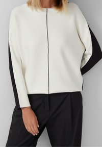 Pull à blocs de couleur blanc et noir avec un col rond et des manches longues, présentant une couture centrale verticale à l'avant.