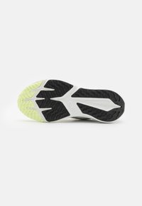 Semelle de chaussure Nike présentant une surface texturée noire avec des accents verts. Le design comprend des rainures profondes pour la traction et une forme distinctive.