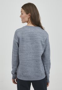 Grå hettegenser laget av teksturert stoff, med lange ermer, rund halsringning, og en ren finish i kanten og mansjettene.