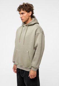 Hoodie aus hellgrauem Stoff mit einer Kängurutasche, gerippten Bündchen und kontrastierenden Zugbandakzenten. Lockere Passform und minimalistisches Design.