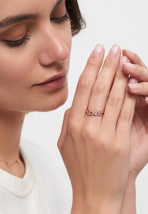 Rose gold ring featuring the word "LOVE" embellished with clear gemstones. Smooth textures and delicate design with a polished finish.
