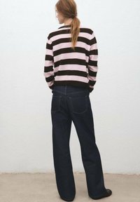 Jersey de punto a rayas marrones y rosas, vista trasera, combinado con unos vaqueros de pierna ancha azul oscuro. El jersey tiene puños y cuello acanalados, y los vaqueros cuentan con bolsillos traseros.