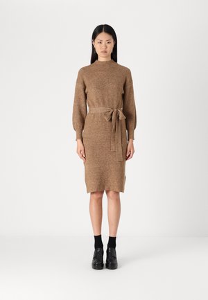 Knit brown dress with long sleeves and a tie belt at the waist. Features a high neck and side slits, paired with black shoes and socks.