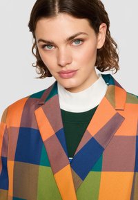 Blazer multicolor con un audaz patrón de cuadros en naranja, azul, verde y marrón, con cuello de muesca y tejido texturizado.