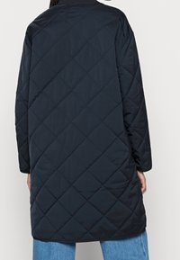 Giubbotto lungo nero trapuntato con motivo a diamante, dotato di maniche lunghe e scollatura rotonda, realizzato in materiale leggero e resistente all'acqua.