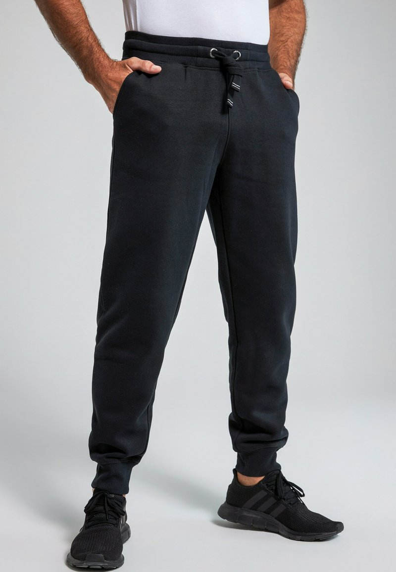 Pantalones de chándal negros con cintura elástica y cordón, con bolsillos laterales y piernas ajustadas. La tela parece suave y texturizada.