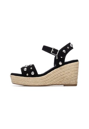 Sandalias cuña de ante negro con tachuelas decorativas plateadas, plataforma de yute trenzado, correa de tobillo ajustable y diseño de punta redondeada.