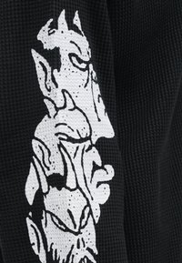 Μαύρος υφασμάτινος ιστός με υφή και έντυπη λευκή σχεδίαση με στυλιζαρισμένα πρόσωπα στοιβαγμένα κάθετα.