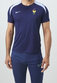 Námořnické sportovní tričko s světle modrými ramenními akcenty, s emblémem kohouta a dvěma hvězdami. V kombinaci s odpovídajícími námořnickými kalhotami.