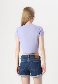 Levanduľové cropped tričko s krátkymi rukávmi, spárované s džínsovými šortkami s rolled hems. Šortky majú na zadnej strane hnedú koženú nášivku s logom značky.
