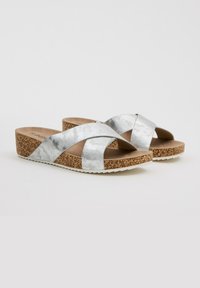 Sandalias con tiras cruzadas plateadas y suela de corcho en cuña, que presentan un diseño de tiras texturizadas y una plantilla marrón lisa. Suela de goma blanca.