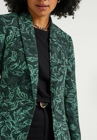 Grön blommönstrad kavaj i texturerat tyg, med slagkrage, enkel knappstängning och framfickor. Svart topp under.