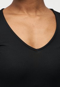 Μαύρο ριμπ τοπ με V-λαιμόκοψη, με υφή στο ύφασμα και εφαρμοστή γραμμή. Το ύφασμα φαίνεται λείο και ελαστικό.