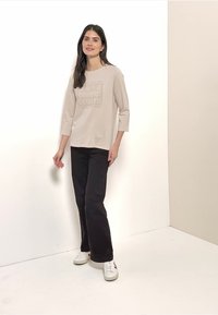 Light beige long-sleeve shirt with a graphic print, paired with black wide-leg pants and white sneakers. Smooth fabric, casual fit.