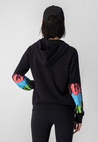 Felpa con cappuccio nera decorata con schizzi colorati di rosa, blu e verde su entrambe le maniche. Tessuto morbido, vestibilità comoda e polsini a coste.