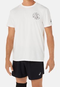 Camiseta de algodón blanca de manga corta, con un pequeño diseño gráfico negro en el pecho y un logotipo en la manga izquierda.