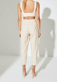 Pantalons beige, ajustés avec une longueur cropped. Tissu doux, texture lisse, devant plat avec poches latérales. Portés avec un crop top de couleur claire.