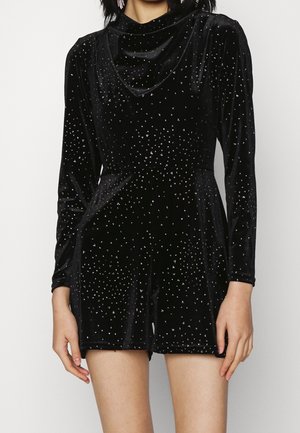 Kvinde iført en langærmet sort velourdragt med små, spredte sølvnitter foran og på shorts.