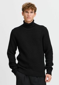 Jersey de punto negro con cuello alto, con un patrón texturizado, puños y dobladillo acanalados. Hecho de una tela suave, presenta un diseño de ajuste holgado.