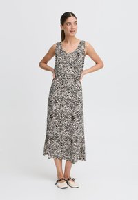 Rochie maxi fără mâneci, neagră și bej, cu un imprimeu animalier abstract, dintr-un material fluid, având un decolteu rotund, purtată cu încălțăminte de culoare deschisă.