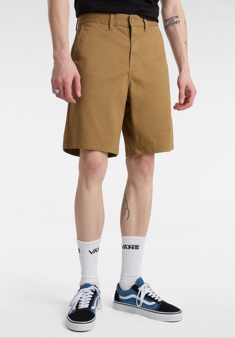 Khaki šortky v uvolněném střihu, s knoflíkovým zapínáním a poutky na opasek. Doplněné o bílé crew ponožky a modré tenisky.