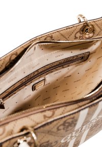 Tan patterned handbag with gold hardware, featuring a zipper closure, multiple compartments, and a branded fabric lining with repeated logo.