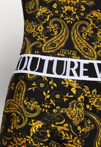 Schwarzer Stoff mit kunstvollen gelben Barock-Blumen- und Paisleymustern, versehen mit einem weißen Bund mit auffälligem schwarzen "COUTURE"-Text.