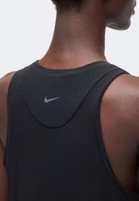 Vue arrière d'une personne portant un haut noir sans manches Nike avec un petit logo Swoosh gris centré sous le cou.