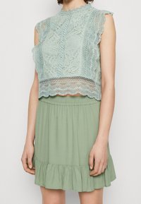 Débardeur en dentelle vert menthe clair avec des bords festonnés et des manches courtes, associé à une jupe à ourlet volanté en tissu léger.