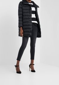 Kvinde iført en sort pufferjakke, sort-og-hvidstribet sweater, sorte cropped skinny jeans og sorte ankelstroppestøvler med høj hæl.
