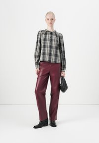 Zwart-wit geblokte blouse met opgestikte mouwen, gecombineerd met bordeauxkleurige nepleren broeken en zwarte leren enkellaarzen met hak. Houdt een zwarte tas vast.