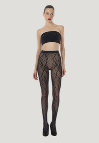 Durchsichtige schwarze Netzstrumpfhosen mit geometrischen Mustern, hohem Bund und glattem Finish, kombiniert mit einem schwarzen Crop-Top und hohen Absätzen.