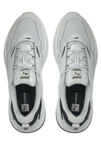 Białe trampki z siateczkową i syntetyczną cholewką, zaokrąglonym noskiem, grubą podeszwą, czarnymi akcentami oraz wyraźnym logo "Puma" na języku.