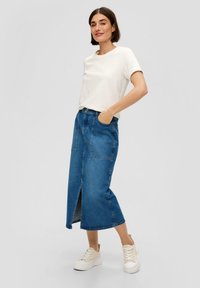 Denim rok, tot de knie met een voorknof, zakken, medium blauwe wassing, gecombineerd met een aansluitend wit t-shirt en lichte sneakers.