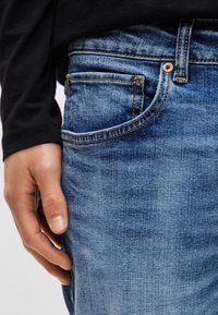 Μπλε τζιν παντελόνι με στενή εφαρμογή, διαθέτει το κλασικό σχέδιο με πέντε τσέπες, λεπτομέρειες με χάλκινες νίπλες και διακριτική ξεθώριαση στο ύφασμα.